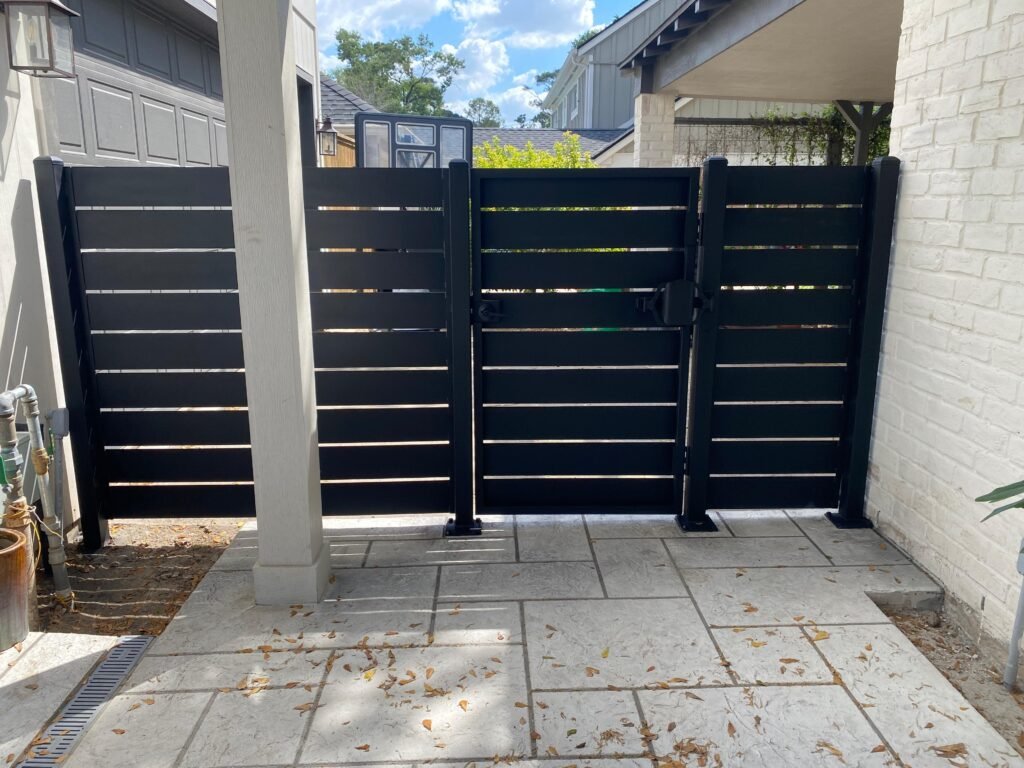 Modern black horizontal slat metal privacy fence with matching pedestrian gate installed in a residential outdoor living area.