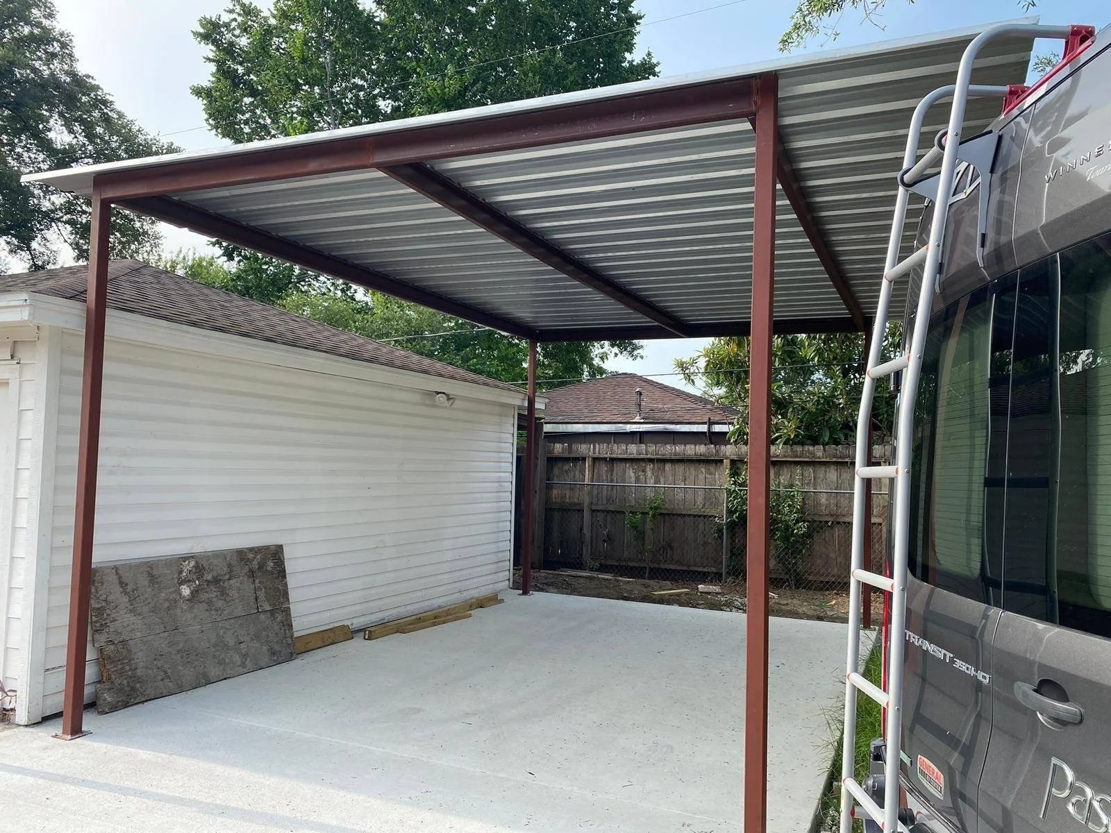 Custom steel carport with metal roof installed over a residential concrete parking area.