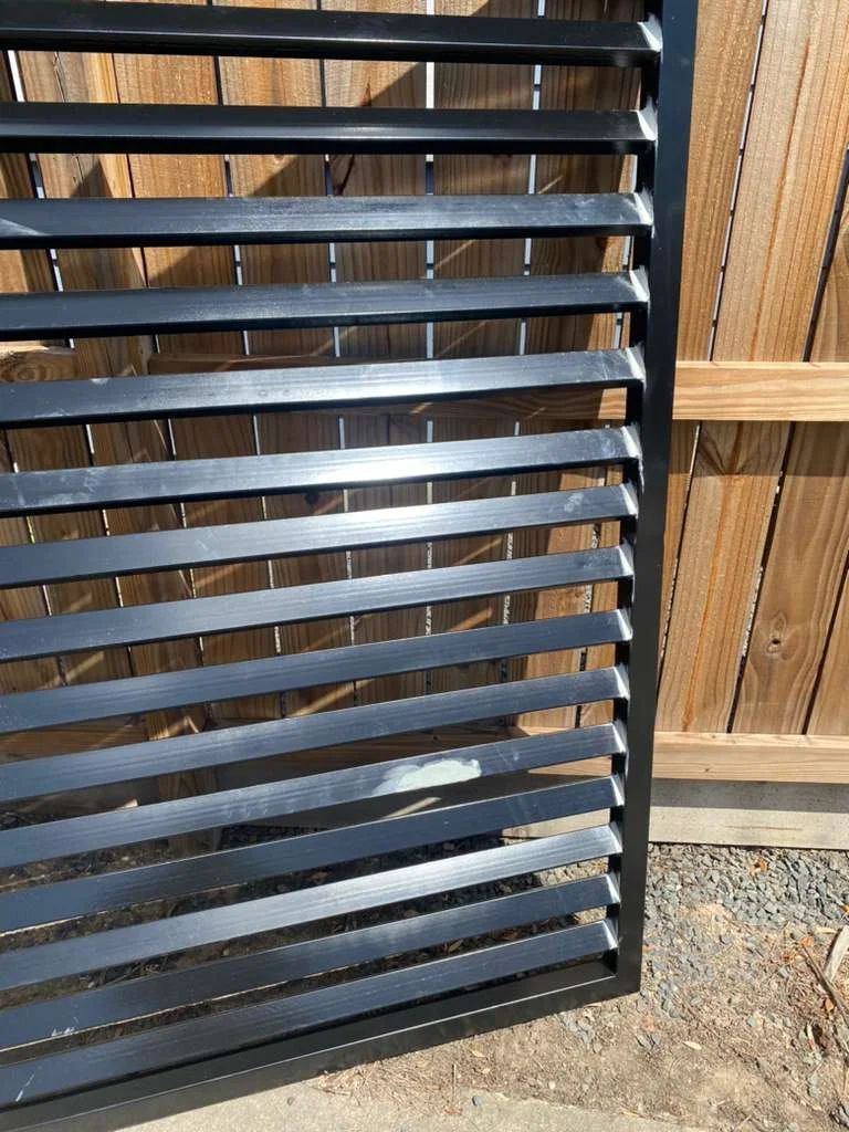 Close-up of a black horizontal slat metal fence panel installed alongside a wooden privacy fence in Houston, TX.